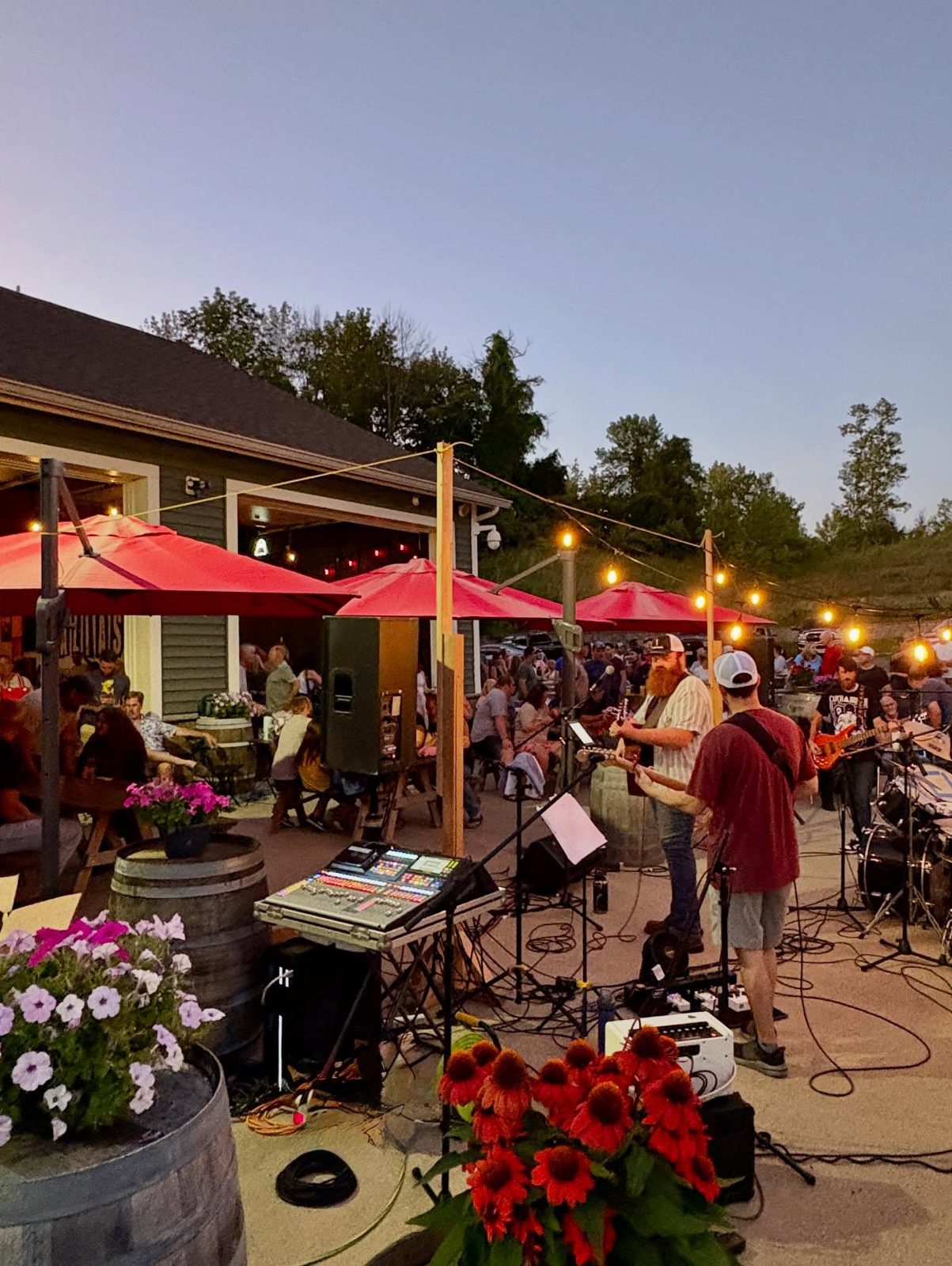 An evening crowd under the umbrellas, band playing, string lights on