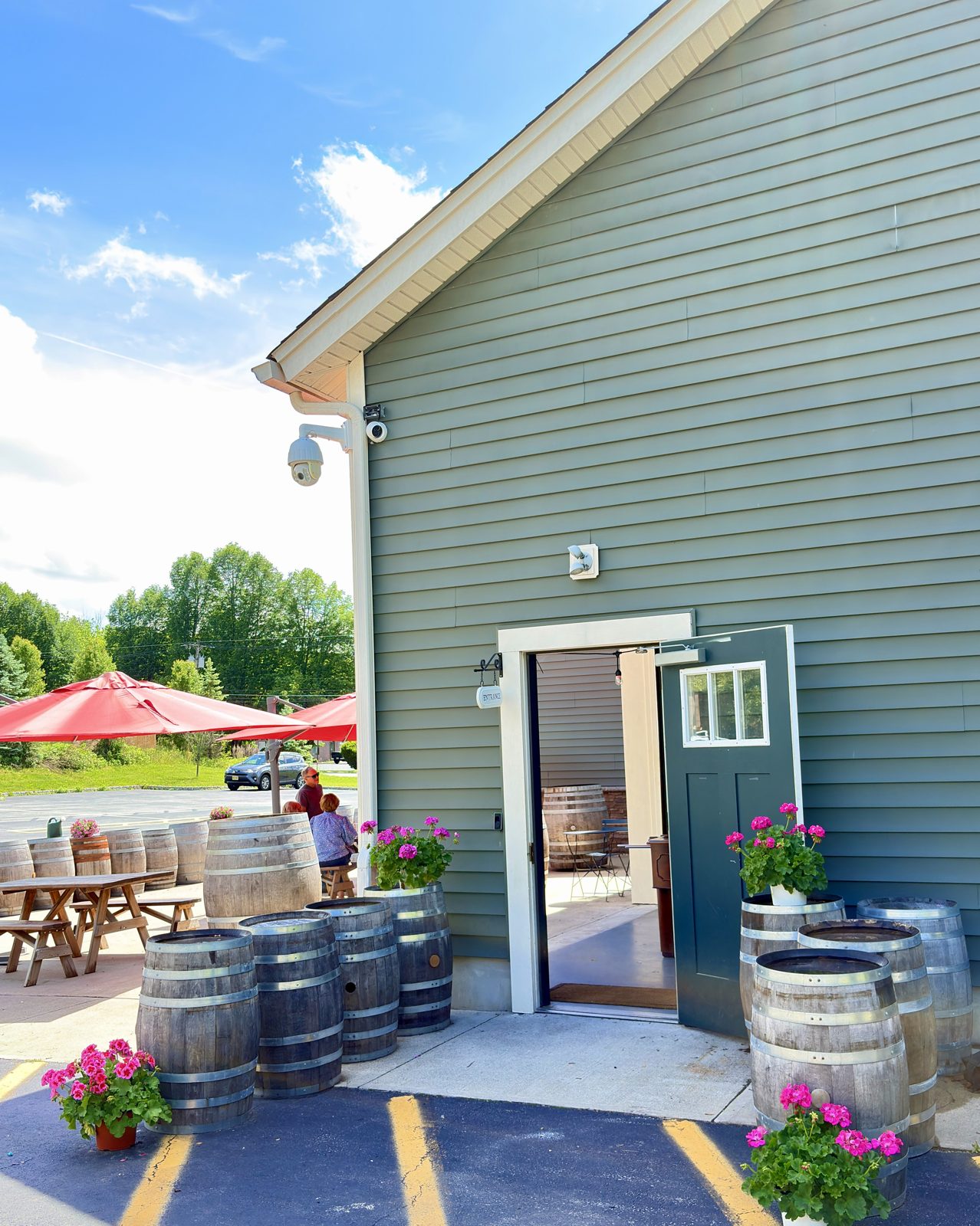 The taproom entrance in summer — flowers, barrels, umbrellas