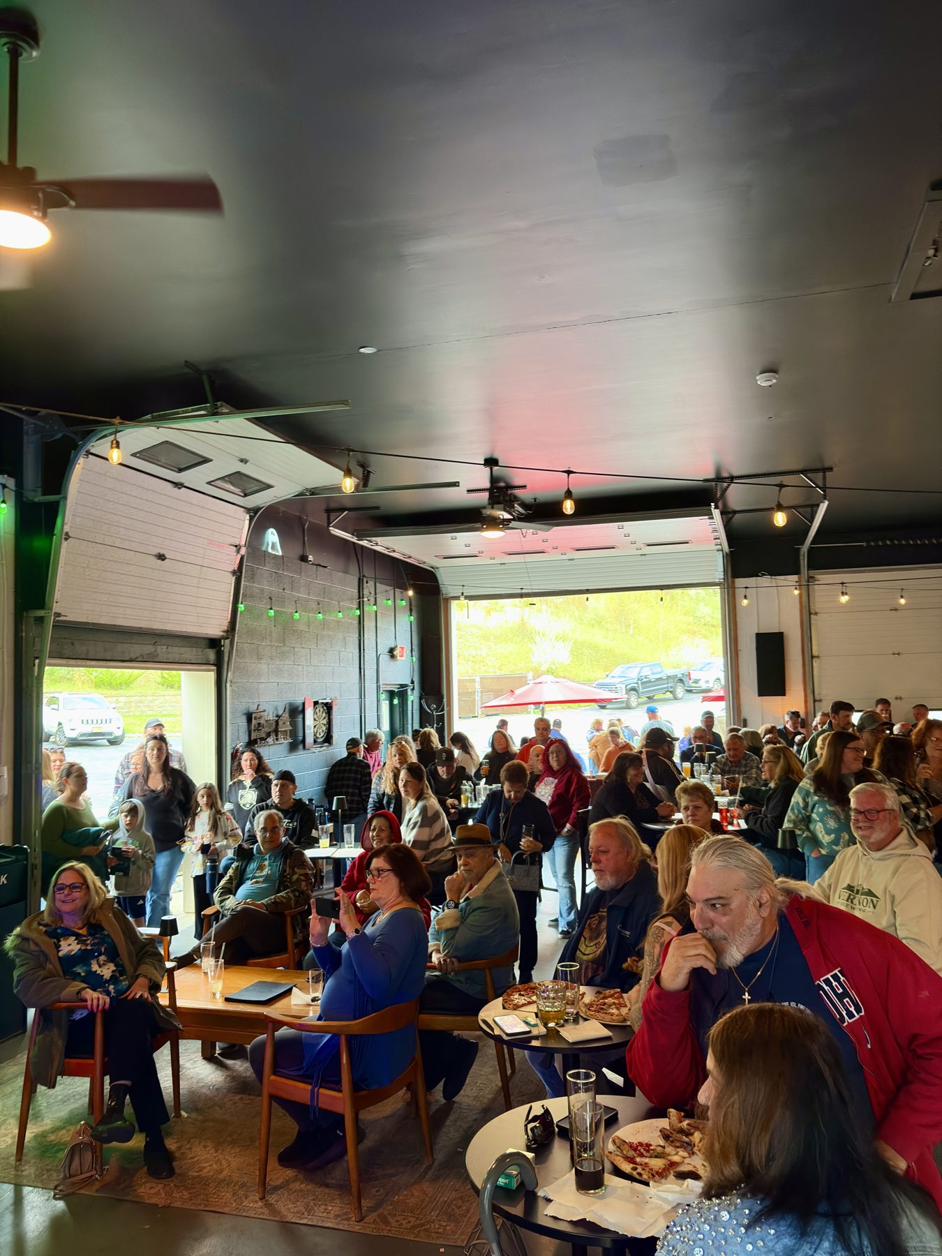 A full taproom, garage doors open to the green hillside
