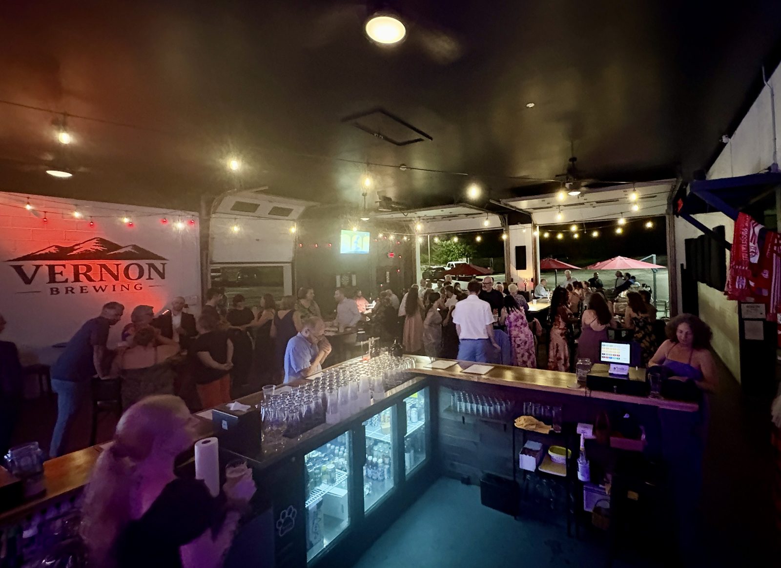 A packed evening party at the bar, Vernon Brewing sign glowing